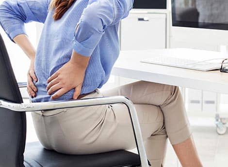 woman holding her lower back in pain as she sits